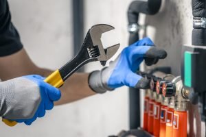a man installs a heating system in a house and checks the pipes with a wrench.